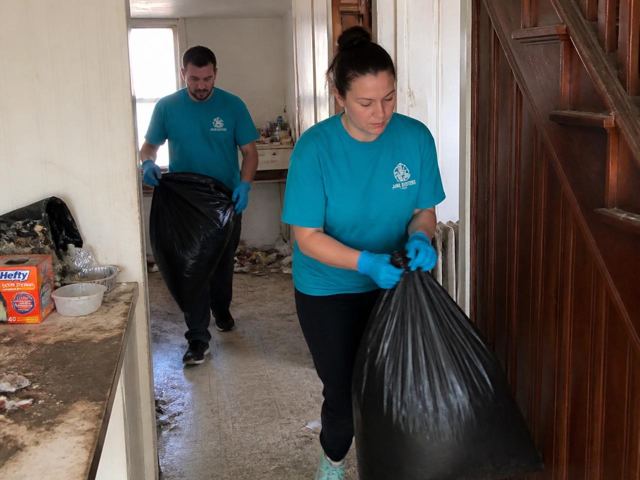 CP Cleaning crew in branded shirts and gloves hauling trash bags out of a cluttered home
