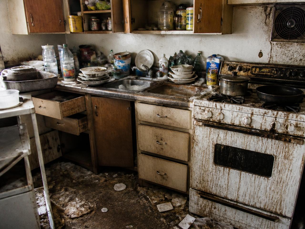 Severely neglected kitchen with grease, grime and piled dishes before deep cleaning